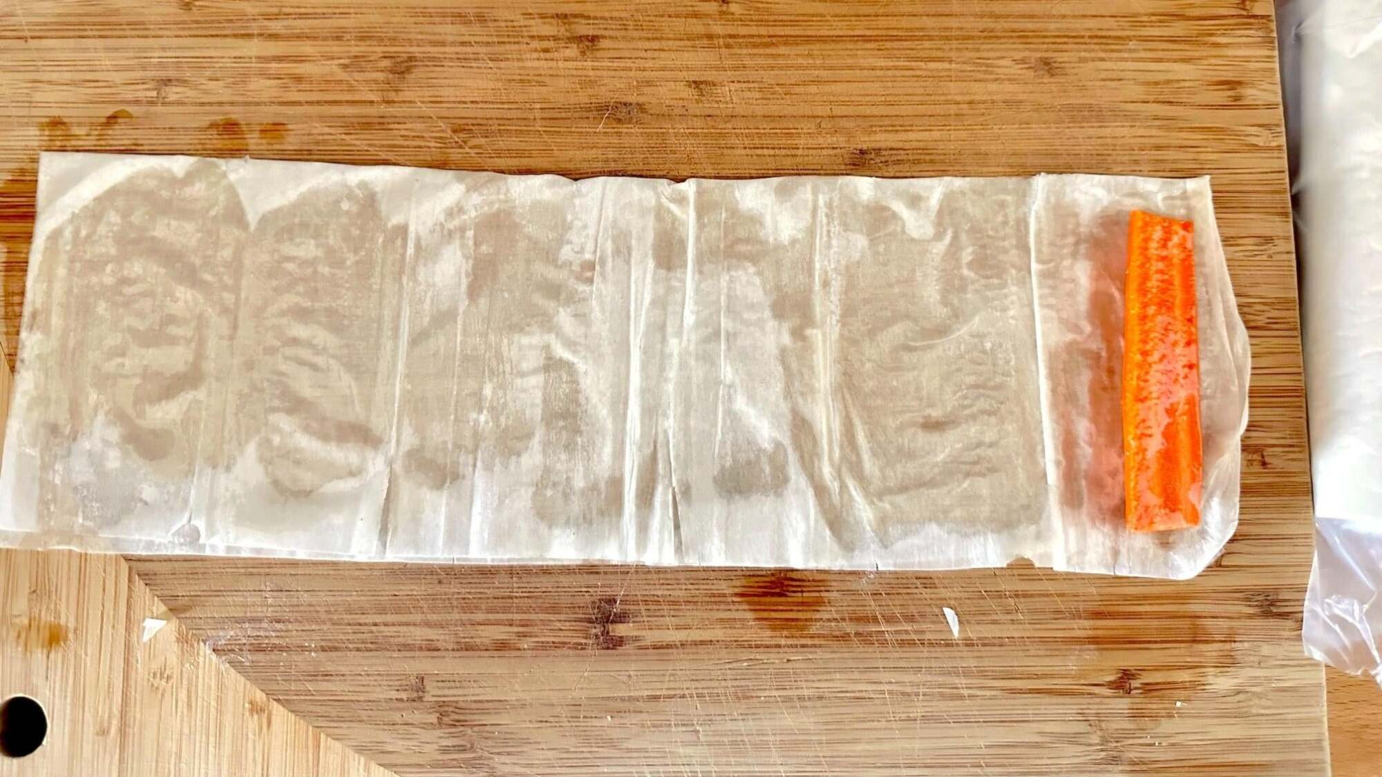 A carrot stick sits on one end of a buttered and folded sheet of phyllo dough.